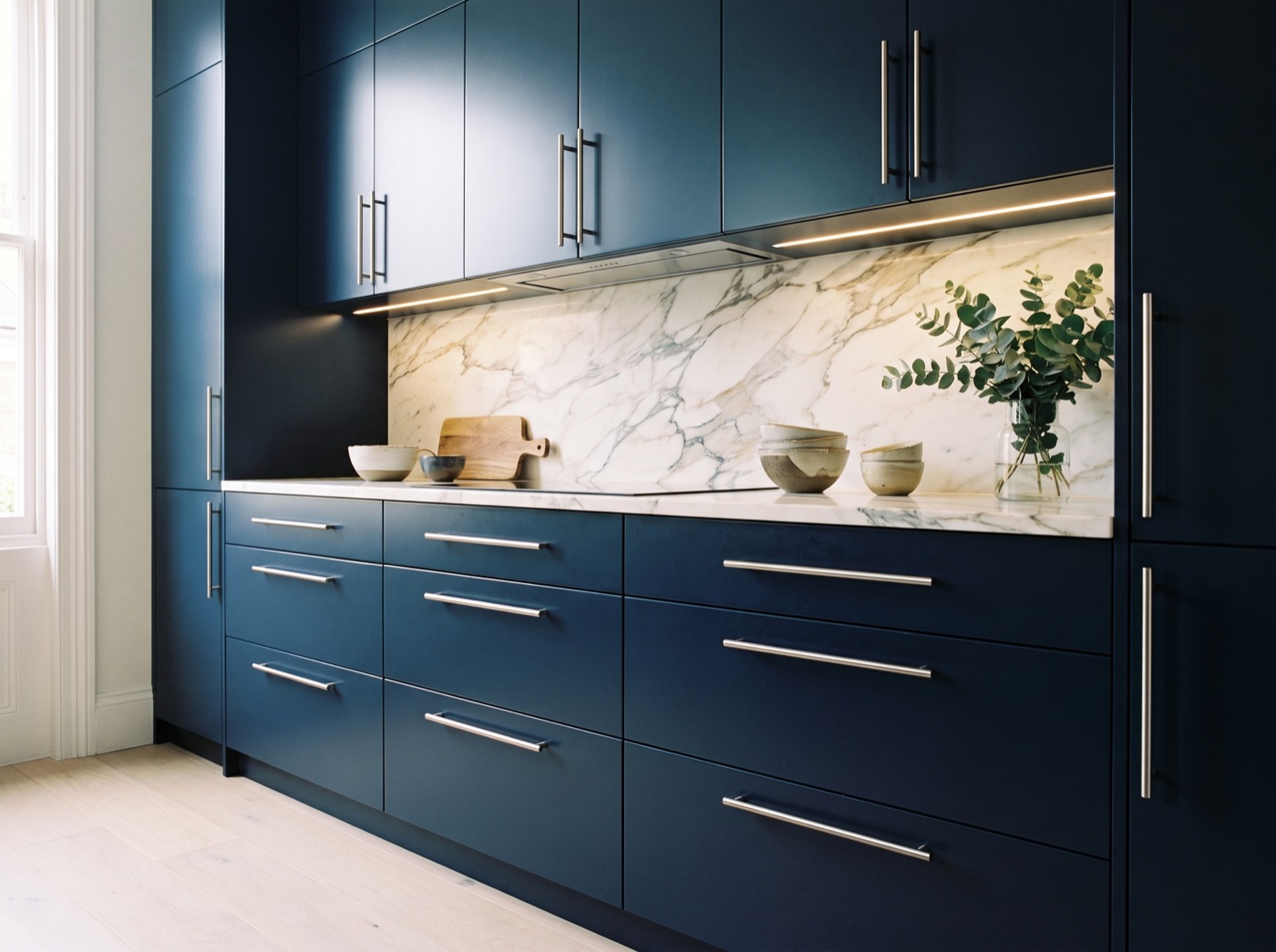 Wellesley Navy flat slab kitchen cabinets in deep navy with brushed nickel bar pulls and a Calacatta marble slab backsplash